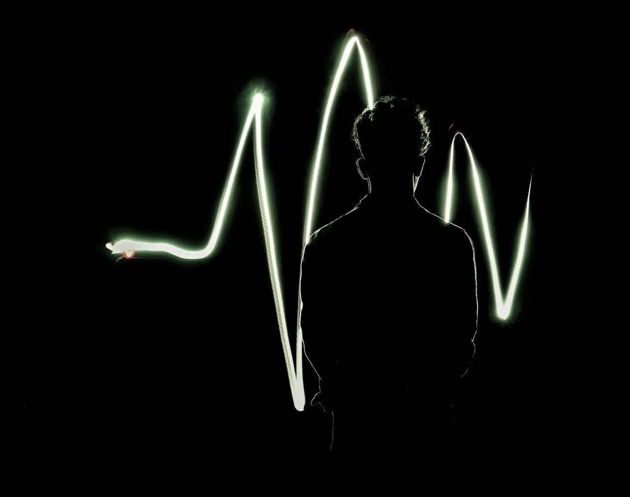 A striking silhouette of a man against vibrant light painting waves on a dark background.